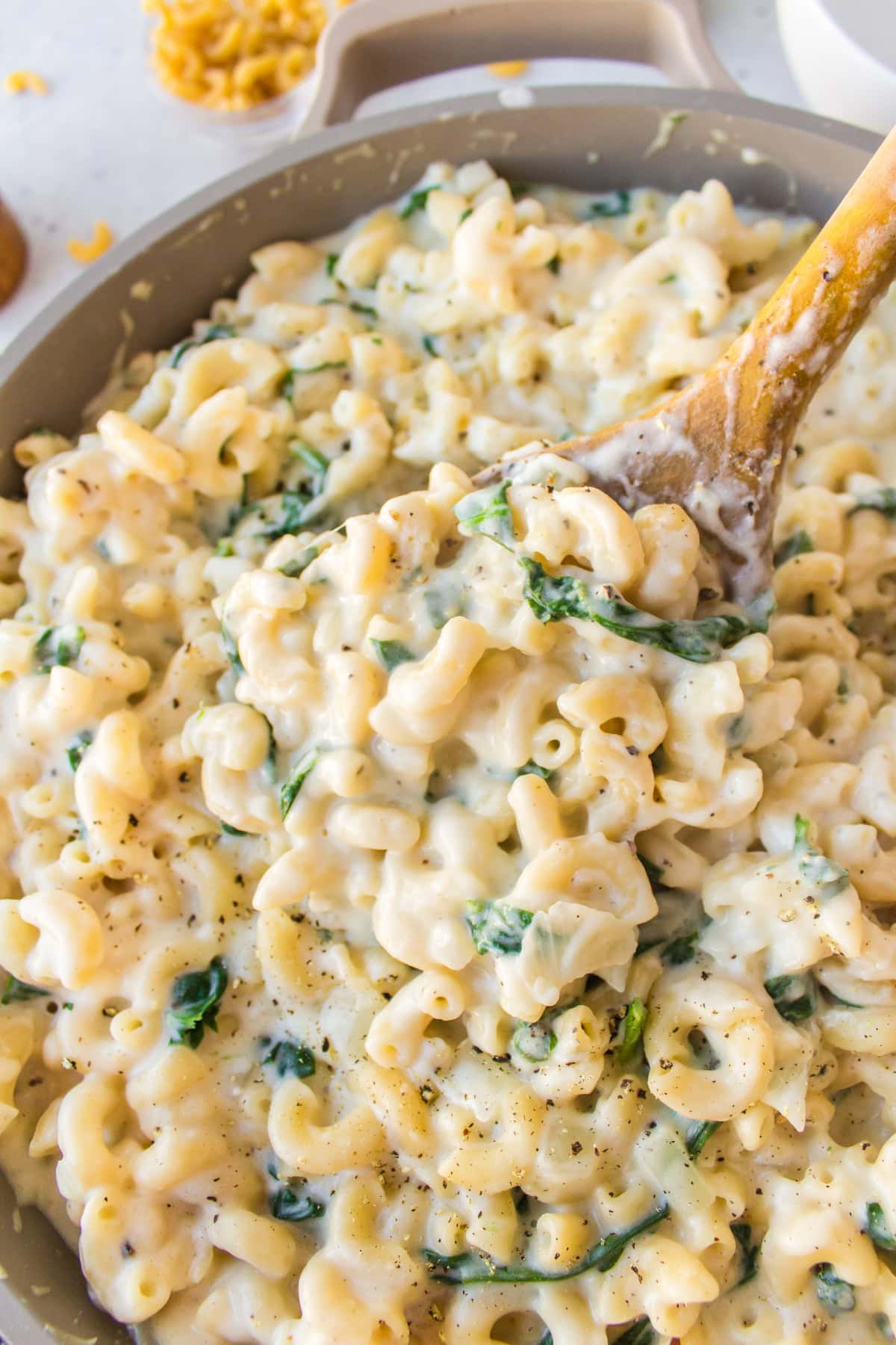 Spinach Mac and Cheese is creamy, cheesy comfort food with fresh spinach and a blend of delicious cheeses. wooden spoon in skillet of spinach mac and cheese