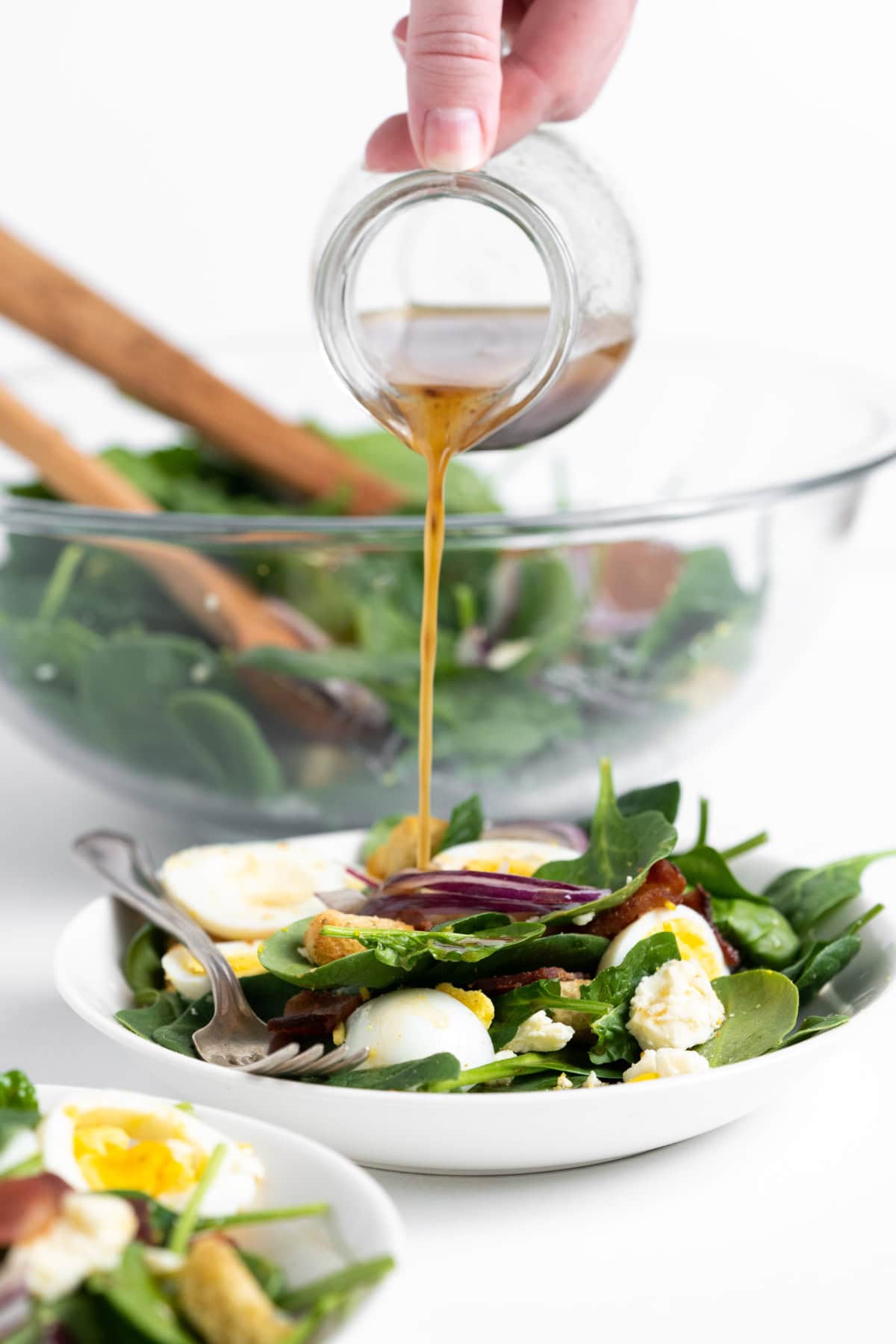 pouring hot bacon dressing onto baby spinach salad