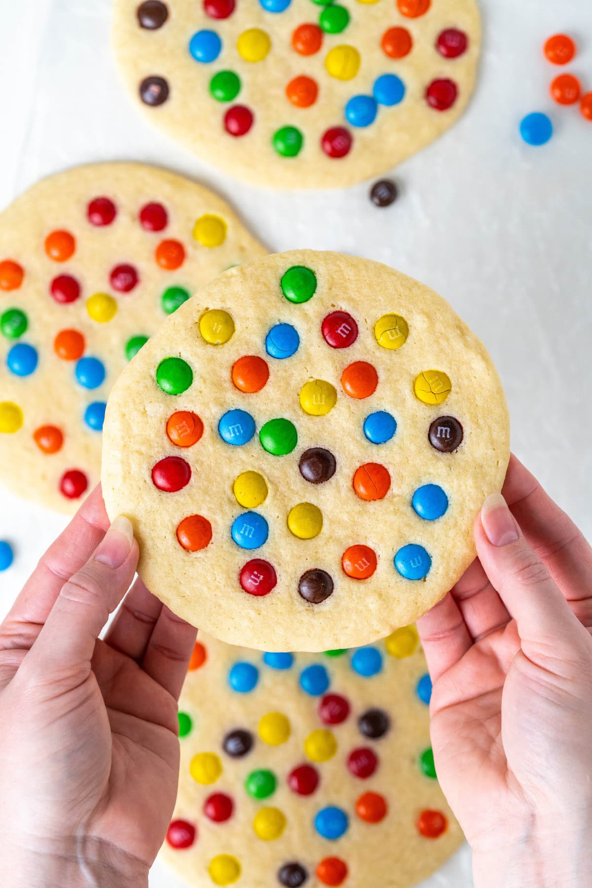 Giant M&M Cookies are soft, chewy and loaded with candy. A bakery-style cookie recipe you can easily make at home. hands holding a giant M&M cookie