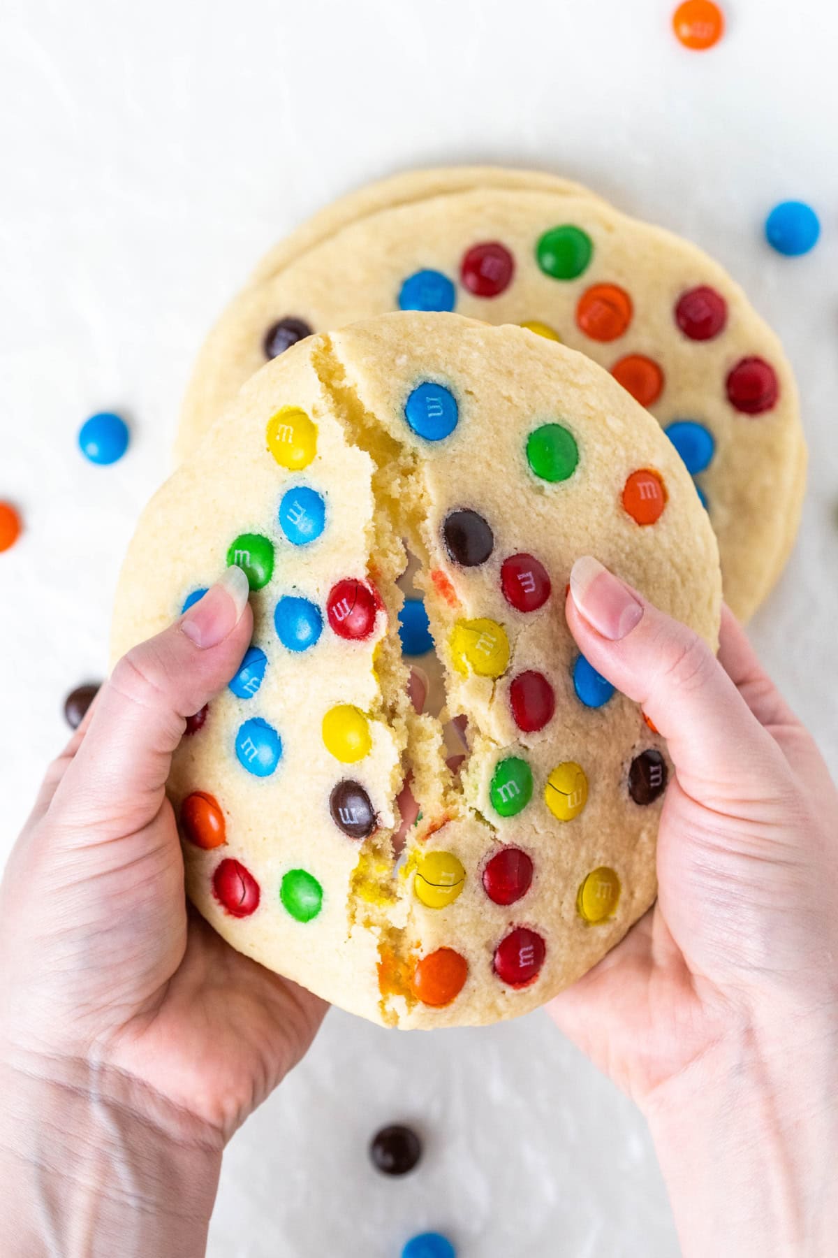 Giant M&M Cookies are soft, chewy and loaded with candy. A bakery-style cookie recipe you can easily make at home. hand breaking apart a giant M&M cookie