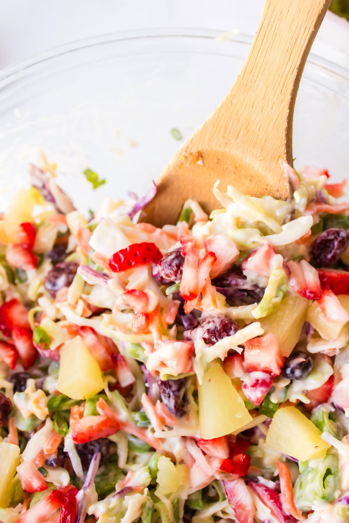 Fruity Coleslaw with strawberries, pineapple and coconut is a sweet, tangy and crunchy side dish perfect for BBQs and summer gatherings. wooden spoon in bowl of fruity coleslaw