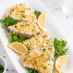 several pieces of swordfish parmesan on a platter with lemon wedges