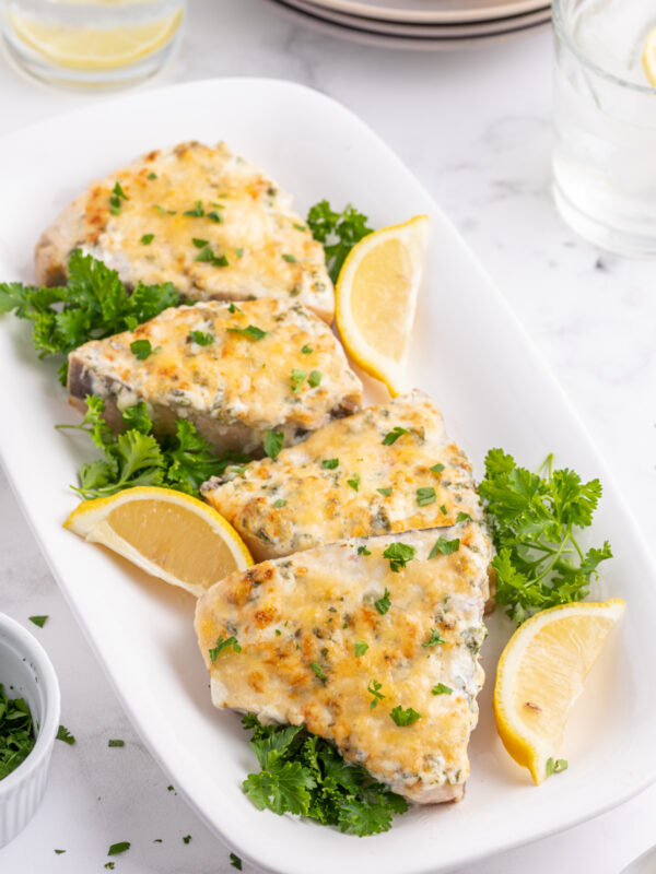 several pieces of swordfish parmesan on a platter with lemon wedges