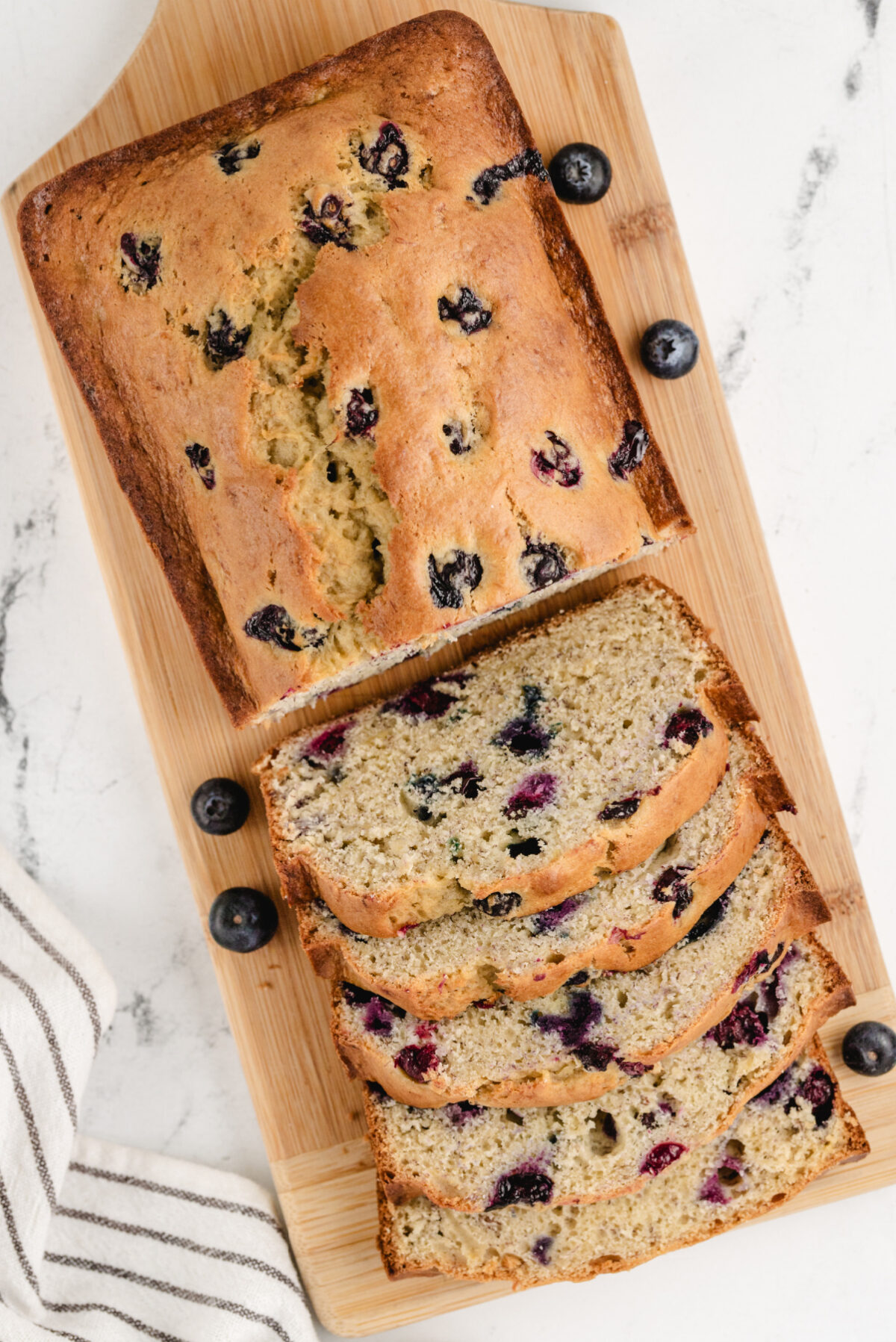 This Blueberry Banana Bread is soft, moist and bursting with juicy blueberries and sweet ripe bananas! It's an easy homemade quick bread that's perfect for breakfast, brunch, snacks or freezing for later. Save this delicious loaf recipe! 🍌🫐 #bananabread #blueberrybananabread #quickbread #breakfastrecipes #homemadebread overhead shot of loaf of blueberry banana bread half sliced