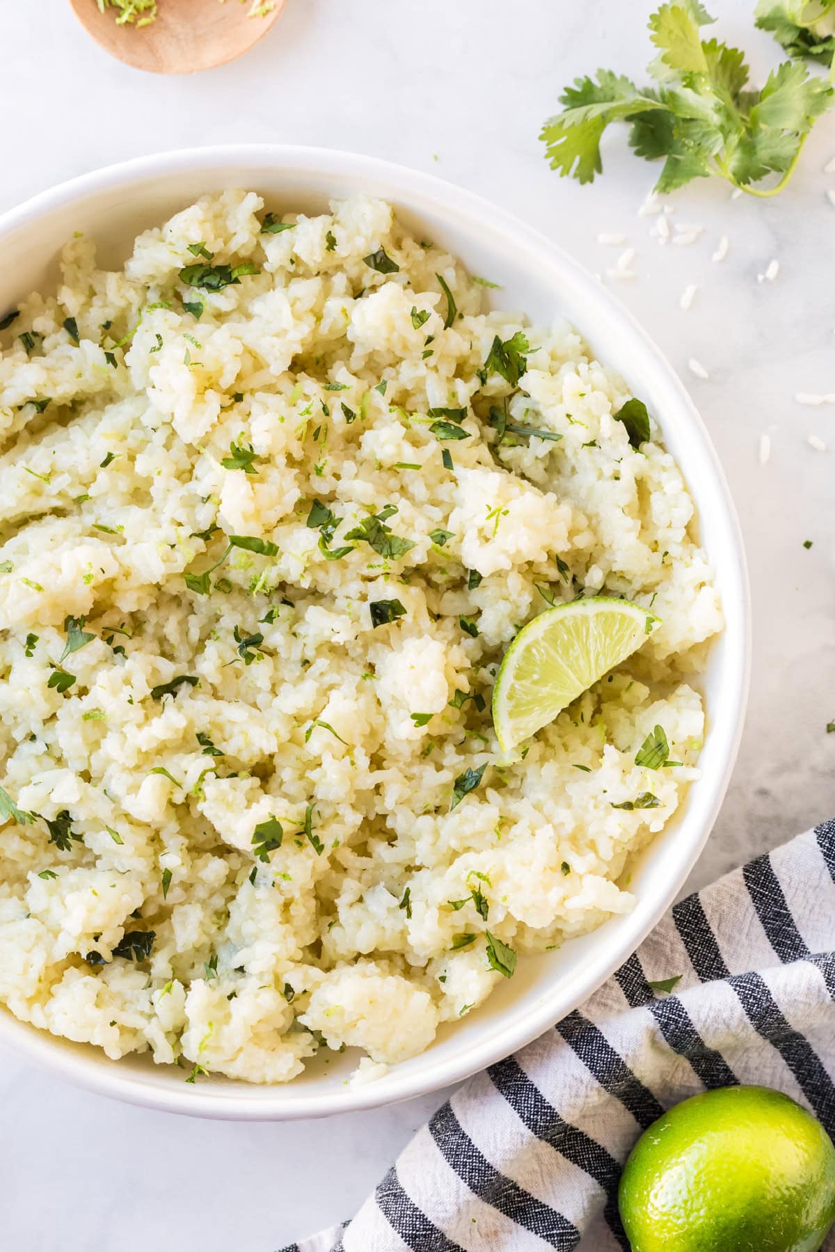 This easy Lime and Cilantro Rice is packed with fresh lime juice, lime zest, cilantro and savory seasonings for incredible flavor. Perfect for tacos, burrito bowls, enchiladas, fajitas and more. Save this restaurant-style rice recipe for your next Mexican dinner night! #cilantrolimerice #mexicanrecipes #rice #sidedish #taconight peek at half a bowl of lime and cilantro rice