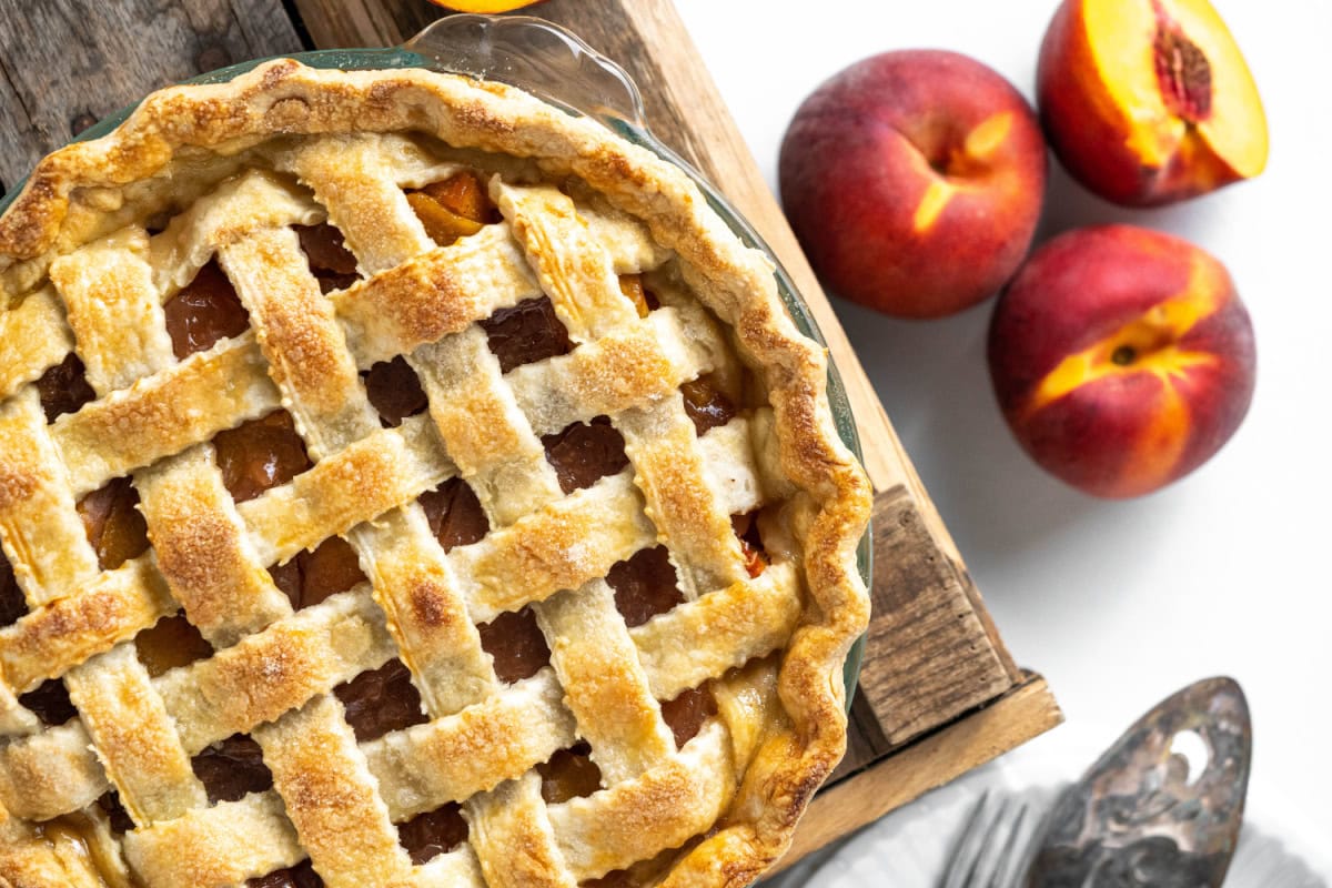 This Fresh Peach Pie Recipe is everything summer baking should be! 🍑 Made with juicy ripe peaches, a flaky homemade butter crust and a gorgeous lattice top, this classic pie is perfect for holidays, BBQs and family gatherings. Save this recipe for peach season! #peachpie #freshpeaches #summerdesserts #pierecipe #homemadepie lattice topped fresh peach pie