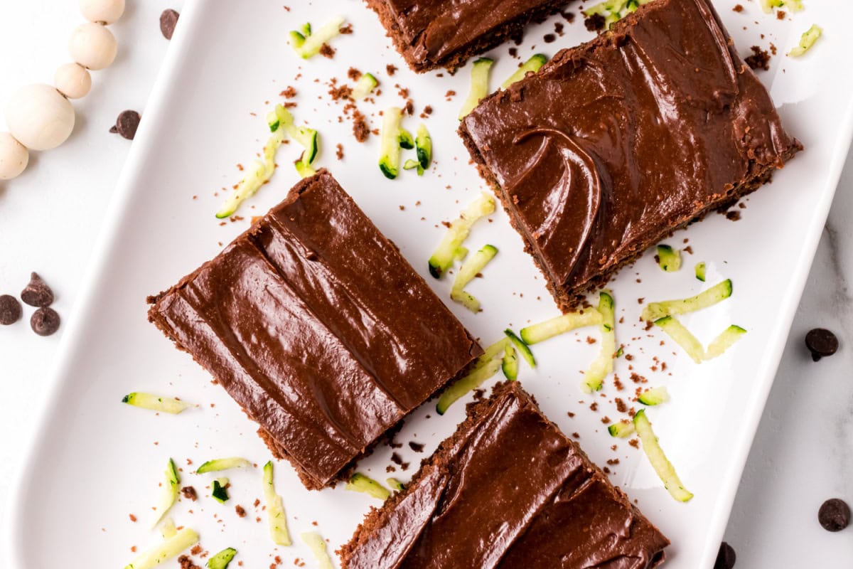 This Chocolate Zucchini Cake is unbelievably moist and rich with chocolate flavor! 🍫 Fresh zucchini keeps the cake soft and tender, while an old-fashioned chocolate marshmallow frosting makes every bite irresistible. Save this easy summer baking recipe! #zucchinicake #chocolatecake #zucchinirecipes #summerbaking #dessertrecipes slices of chocolate zucchini cake overhead shot