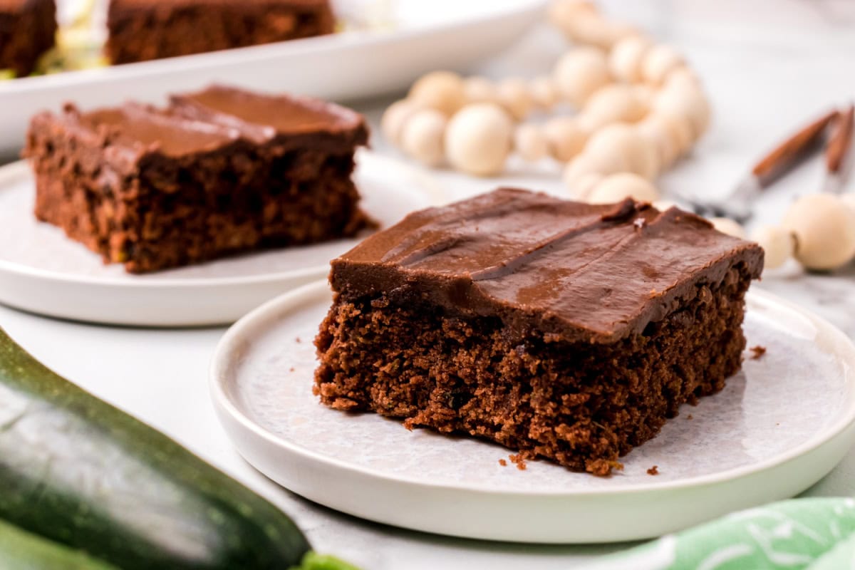 This Chocolate Zucchini Cake is unbelievably moist and rich with chocolate flavor! 🍫 Fresh zucchini keeps the cake soft and tender, while an old-fashioned chocolate marshmallow frosting makes every bite irresistible. Save this easy summer baking recipe! #zucchinicake #chocolatecake #zucchinirecipes #summerbaking #dessertrecipes slice of chocolate zucchini cake