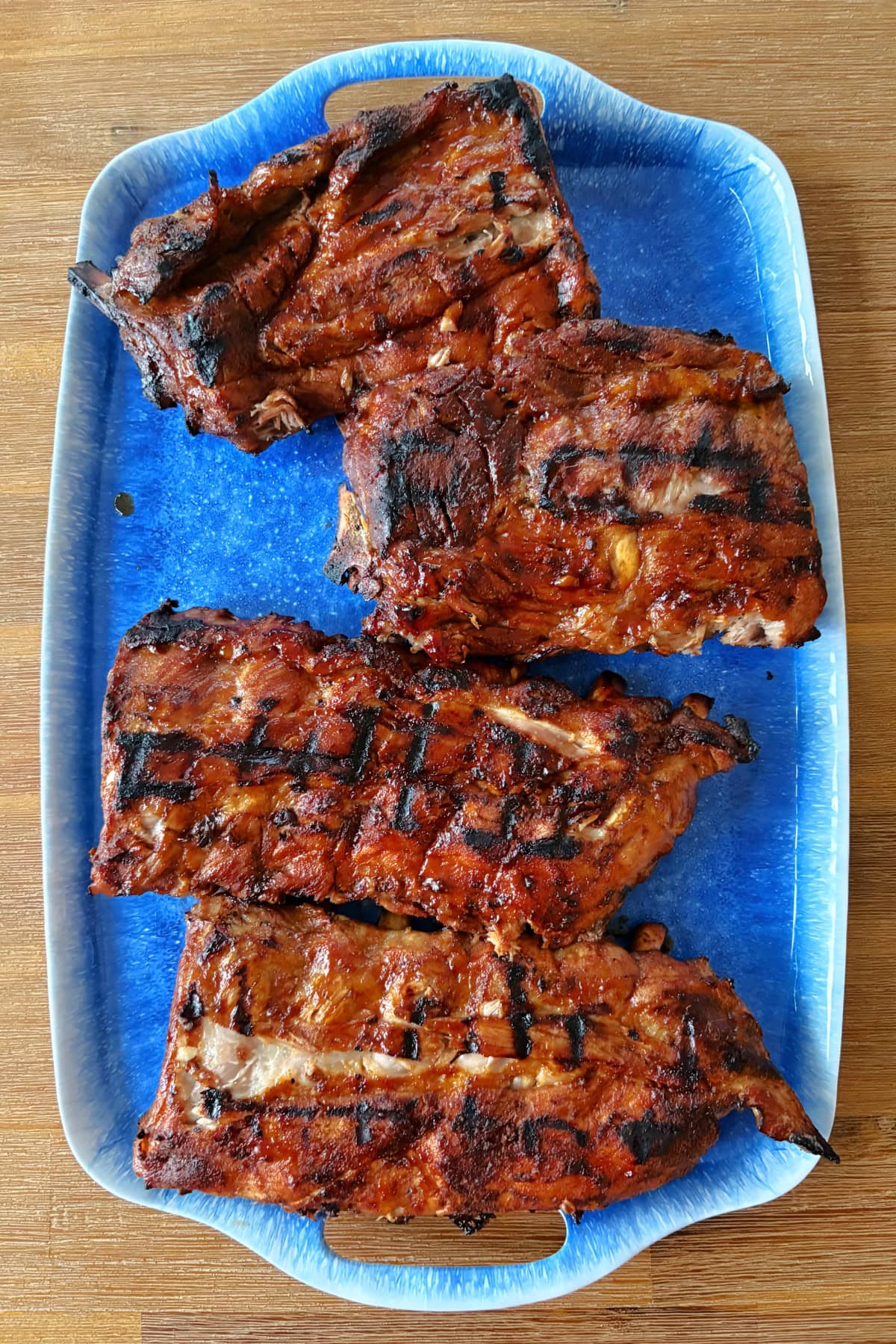 These Dr. Pepper Ribs are fall-apart tender and loaded with flavor! Baby back ribs are marinated in Dr. Pepper, baked until tender and finished on the grill with a sticky homemade Dr. Pepper BBQ sauce. An easy rib recipe for summer cookouts, Father's Day and backyard BBQs. dr pepper ribs on a blue platter