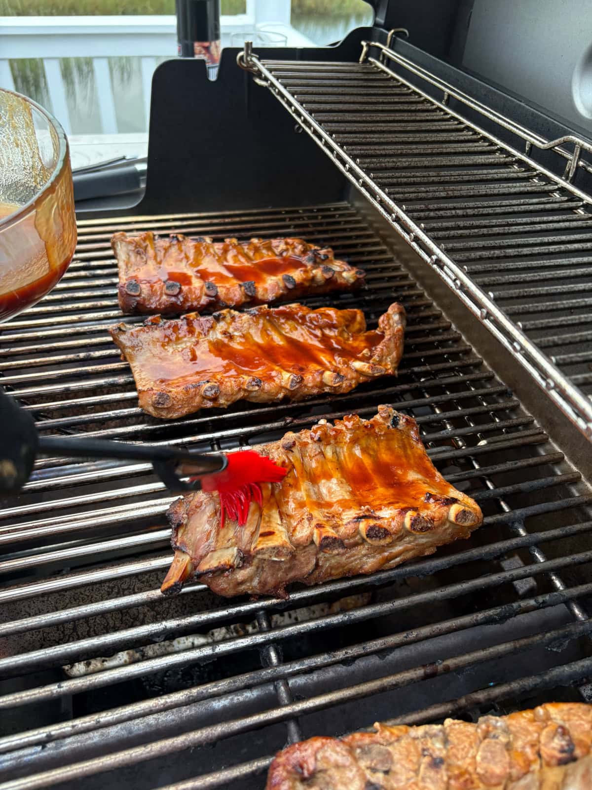 These Dr. Pepper Ribs are fall-apart tender and loaded with flavor! Baby back ribs are marinated in Dr. Pepper, baked until tender and finished on the grill with a sticky homemade Dr. Pepper BBQ sauce. An easy rib recipe for summer cookouts, Father's Day and backyard BBQs. brushing sauce onto grilling ribs