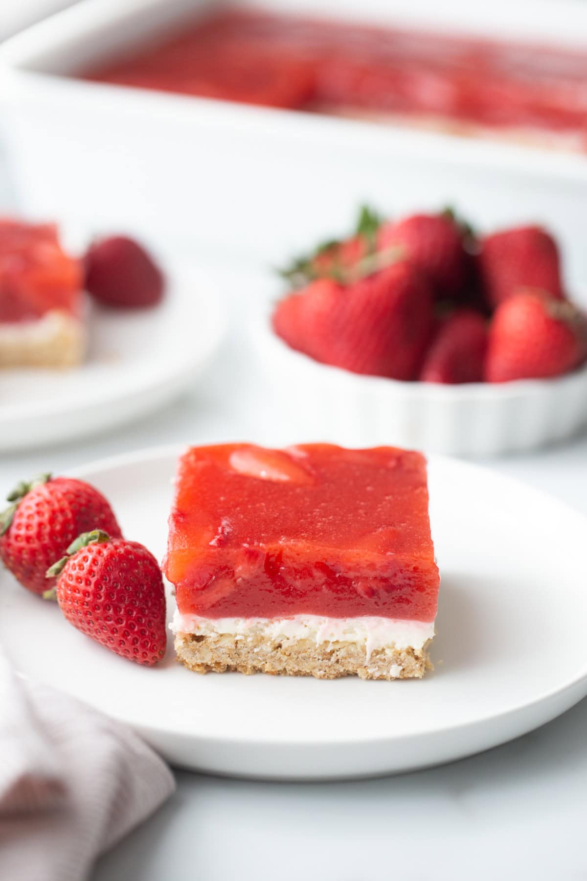 This Old Fashioned Strawberry Pretzel Salad is a timeless favorite! 🍓 Made with a buttery pretzel crust, fluffy cream cheese layer and a homemade strawberry topping with real strawberries, it's the perfect make-ahead dessert for holidays, potlucks and summer parties. Save this classic recipe! #strawberrypretzelsalad #strawberrydessert #potluckrecipes #summerdesserts #vintagerecipes slice of old fashioned strawberry pretzel salad on plate