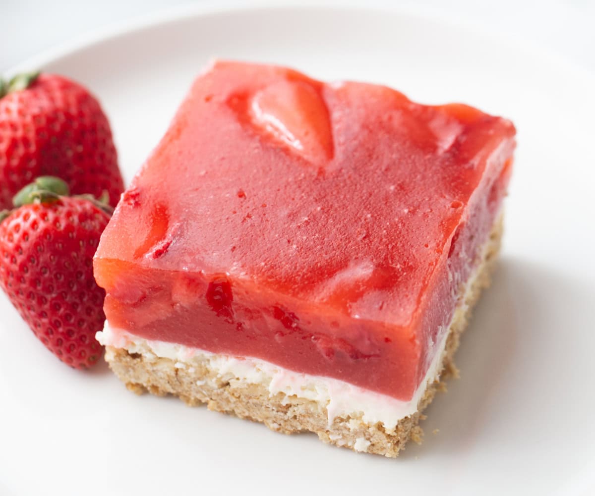 This Old Fashioned Strawberry Pretzel Salad is a timeless favorite! 🍓 Made with a buttery pretzel crust, fluffy cream cheese layer and a homemade strawberry topping with real strawberries, it's the perfect make-ahead dessert for holidays, potlucks and summer parties. Save this classic recipe! #strawberrypretzelsalad #strawberrydessert #potluckrecipes #summerdesserts #vintagerecipes slice of old fashioned strawberry pretel salad
