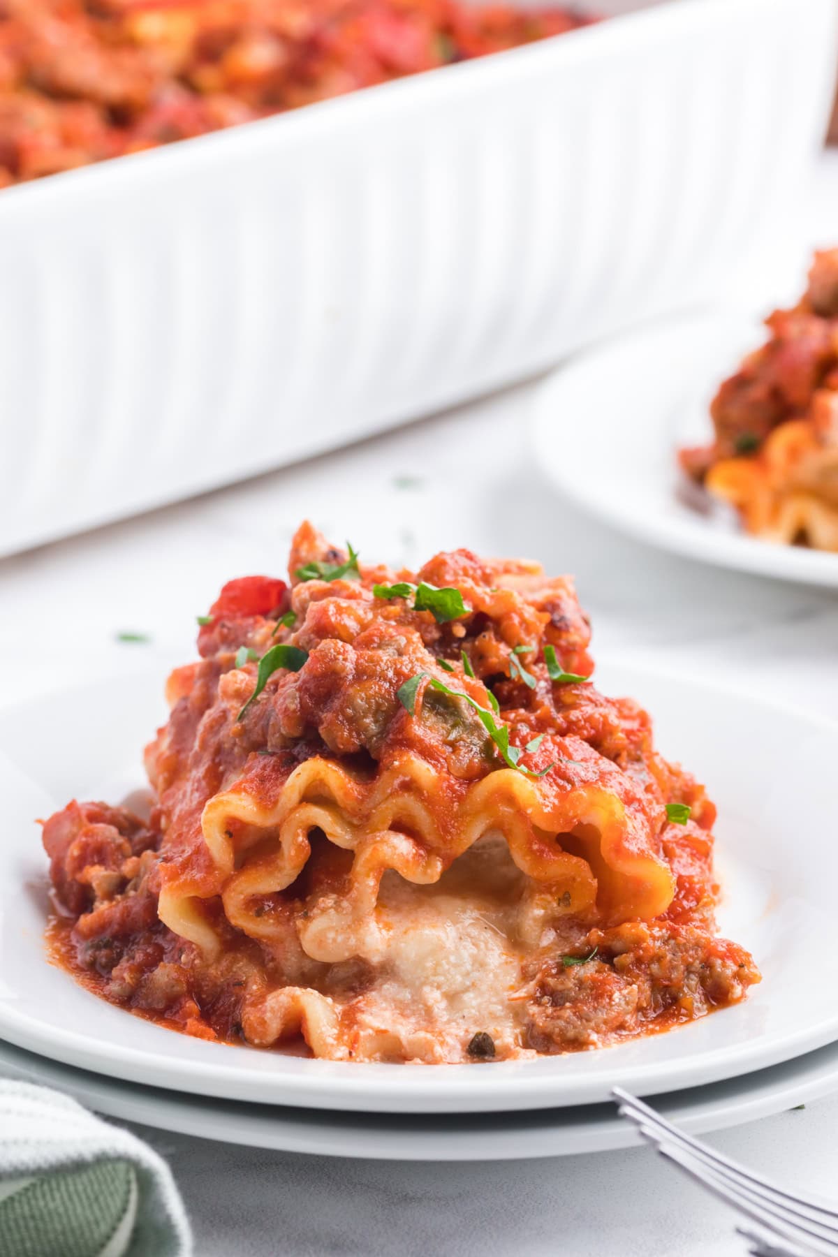 These easy Italian Sausage Lasagna Roll Ups are filled with ricotta, Parmesan and mozzarella, rolled up and baked in a hearty Italian sausage marinara sauce. A cheesy, comforting family dinner that's easy to make ahead and freezer-friendly, too! Save this easy lasagna recipe for weeknight dinners, Sunday supper or entertaining. one Italian Sausage Lasagna Roll Ups on a plate