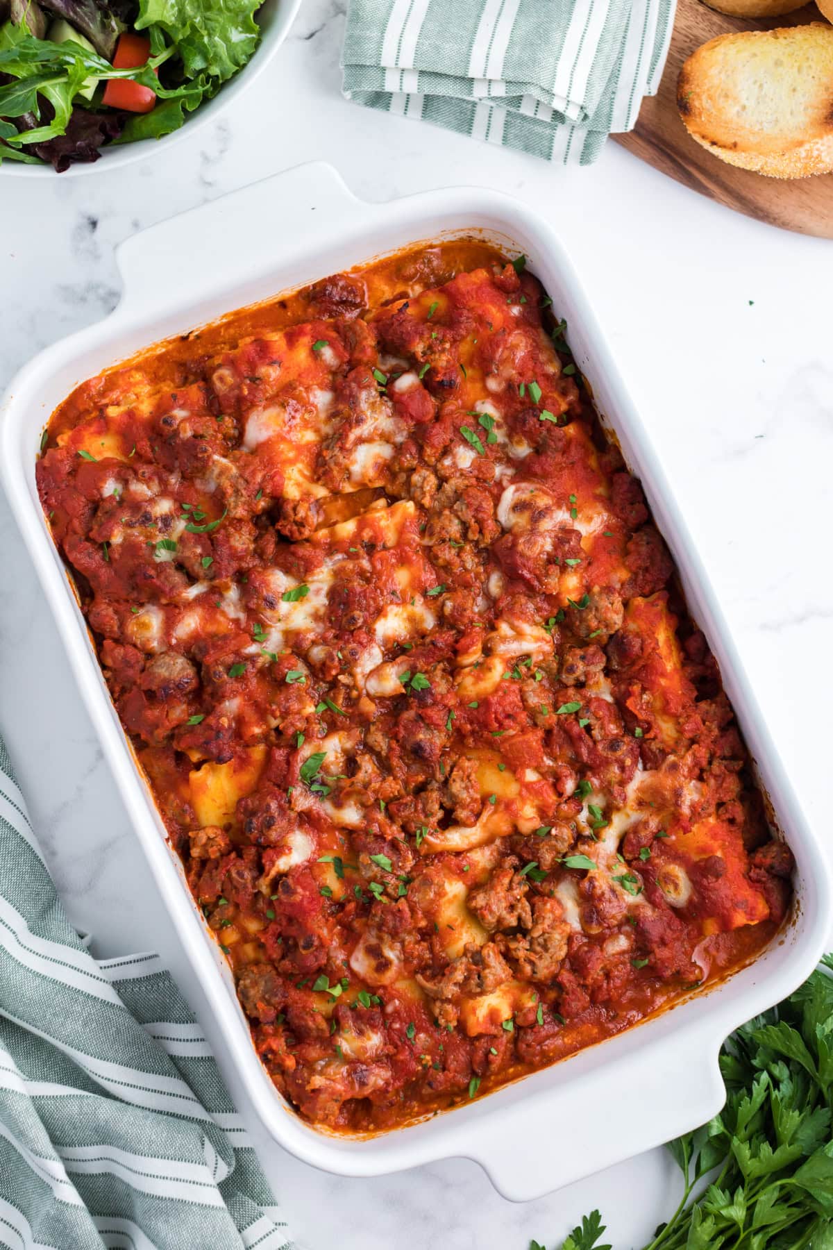 These easy Italian Sausage Lasagna Roll Ups are filled with ricotta, Parmesan and mozzarella, rolled up and baked in a hearty Italian sausage marinara sauce. A cheesy, comforting family dinner that's easy to make ahead and freezer-friendly, too! Save this easy lasagna recipe for weeknight dinners, Sunday supper or entertaining. overhead shot of Italian Sausage Lasagna Roll Ups in white casserole dish