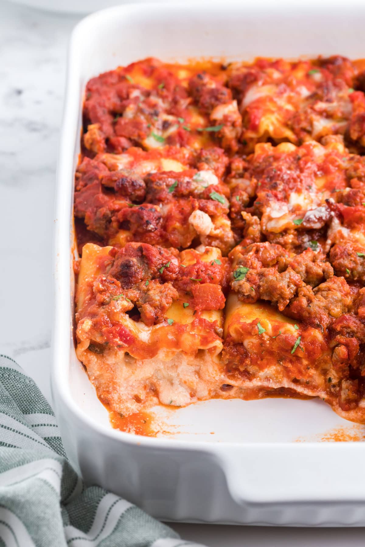These easy Italian Sausage Lasagna Roll Ups are filled with ricotta, Parmesan and mozzarella, rolled up and baked in a hearty Italian sausage marinara sauce. A cheesy, comforting family dinner that's easy to make ahead and freezer-friendly, too! Save this easy lasagna recipe for weeknight dinners, Sunday supper or entertaining. Italian Sausage Lasagna Roll Ups in Casserole Dish with some taken out