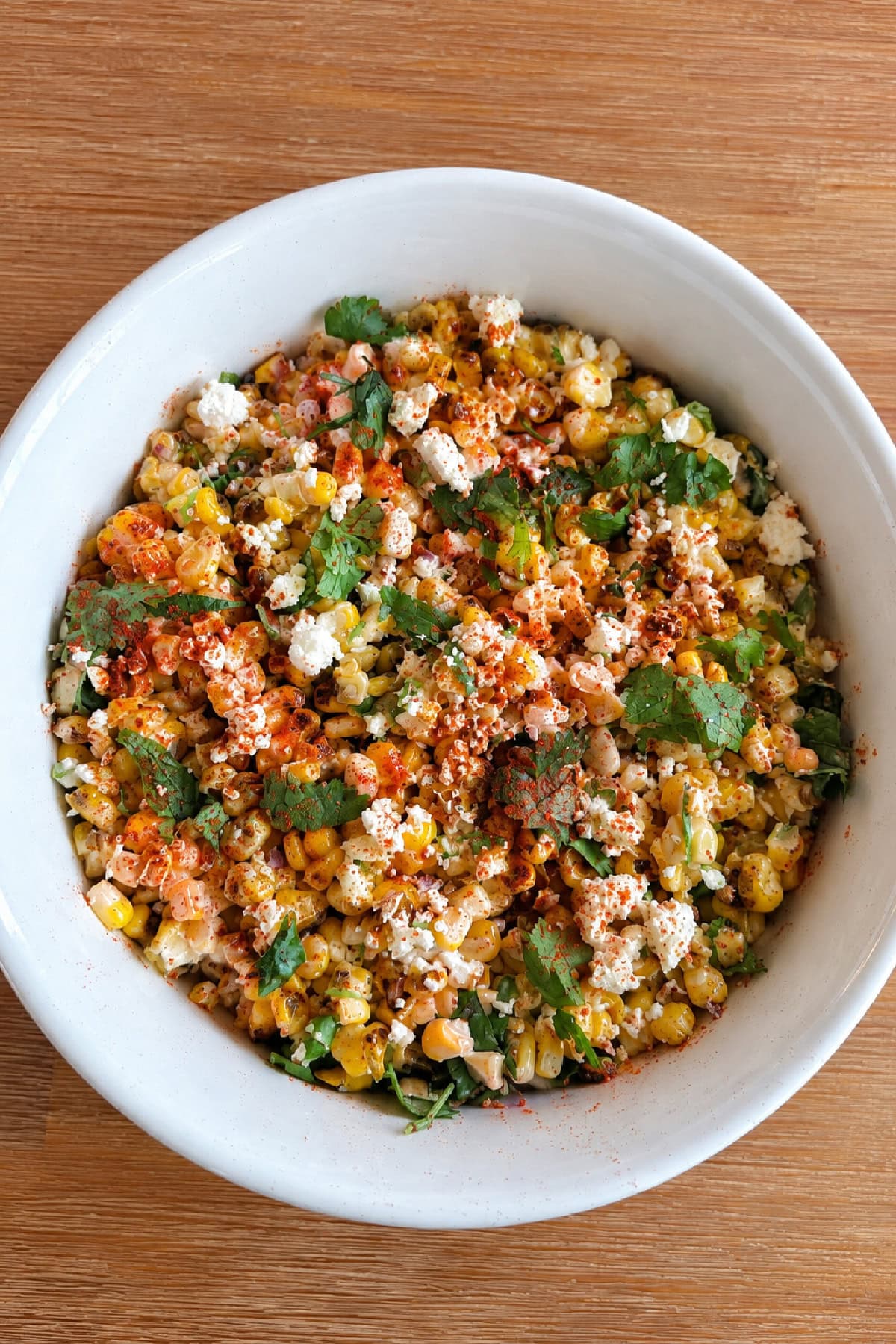 This easy Mexican Street Corn Salad combines lightly charred corn with Cotija cheese, cilantro, green onions and a creamy lime dressing. Make it with fresh, frozen or canned corn for an easy summer side dish that's perfect for tacos, BBQs, potlucks and cookouts. mexican street corn salad in white bowl