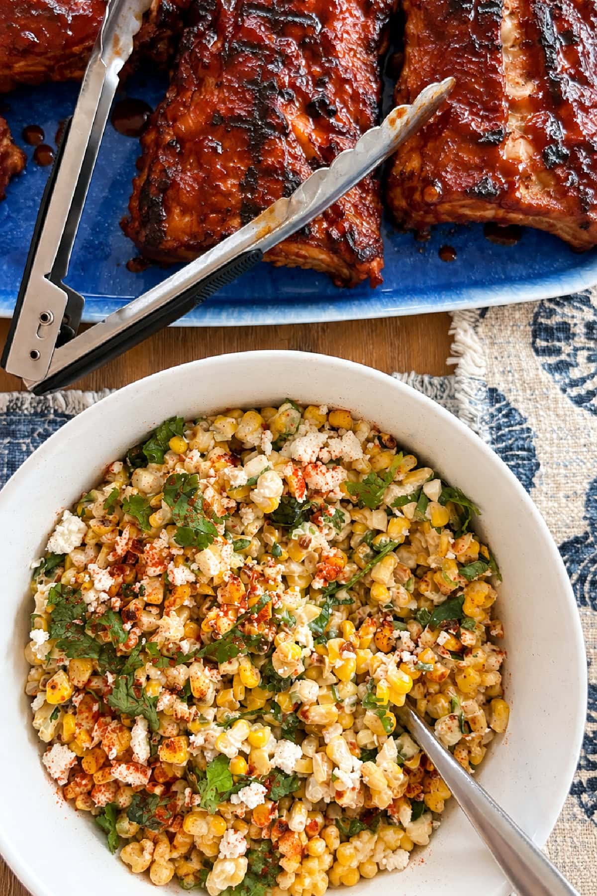 This easy Mexican Street Corn Salad combines lightly charred corn with Cotija cheese, cilantro, green onions and a creamy lime dressing. Make it with fresh, frozen or canned corn for an easy summer side dish that's perfect for tacos, BBQs, potlucks and cookouts. mexican street corn salad in bowl with ribs