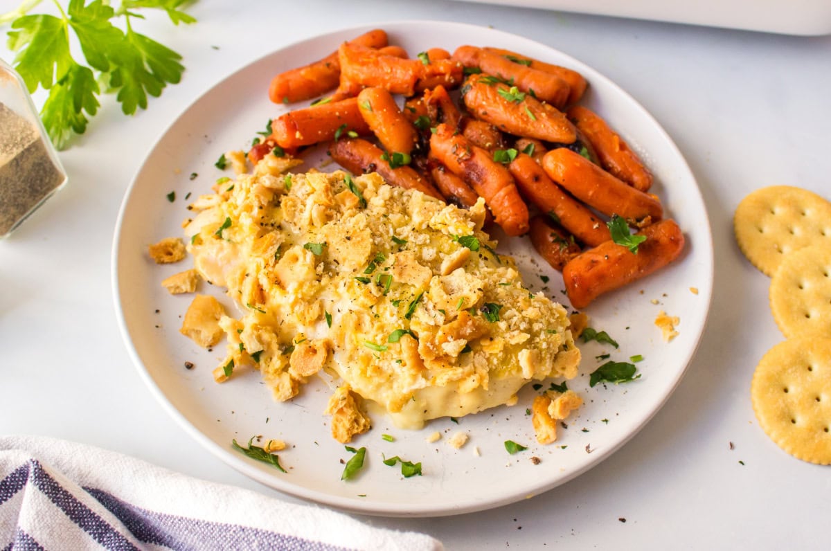 This easy Swiss Cheese Chicken recipe is the perfect comfort-food dinner! Chicken breasts are topped with Swiss cheese, a creamy sauce and buttery Ritz cracker crumbs, then baked until tender and golden. An easy 45-minute chicken dinner that's great for busy weeknights. serving of swiss cheese chicken on plate