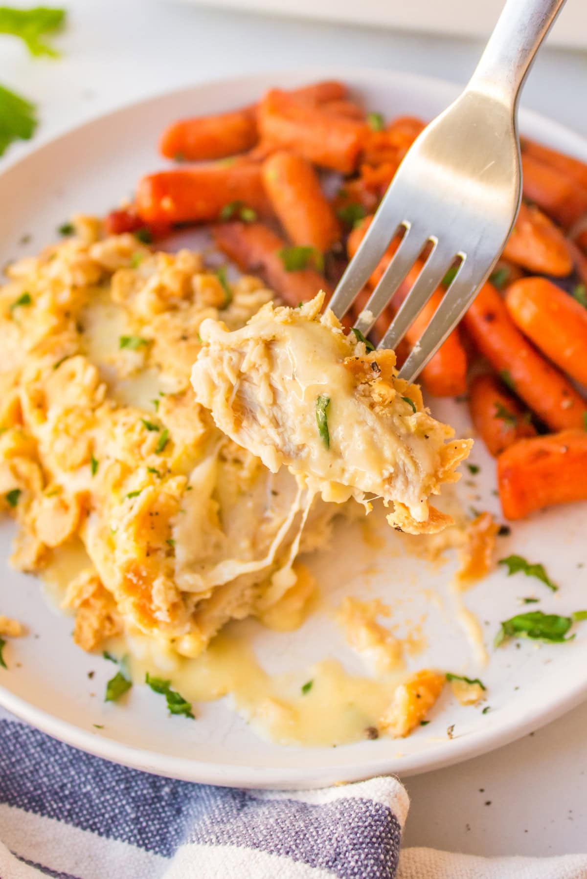 This easy Swiss Cheese Chicken recipe is the perfect comfort-food dinner! Chicken breasts are topped with Swiss cheese, a creamy sauce and buttery Ritz cracker crumbs, then baked until tender and golden. An easy 45-minute chicken dinner that's great for busy weeknights. fork taking up bite of swiss cheese chicken on plate