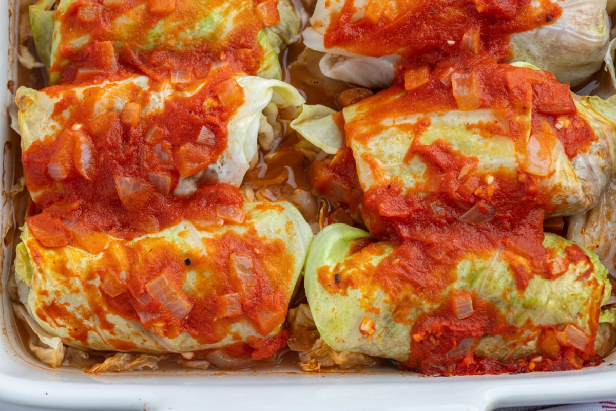 These homemade Polish Cabbage Rolls (Golabki) are the ultimate comfort food! Tender Savoy cabbage leaves are filled with ground beef, rice and seasoned tomato sauce, then baked until tender. Serve with sour cream and applesauce for a delicious old-fashioned family dinner. Save this recipe for a cozy weekend meal! close up of cooked polish cabbage rolls