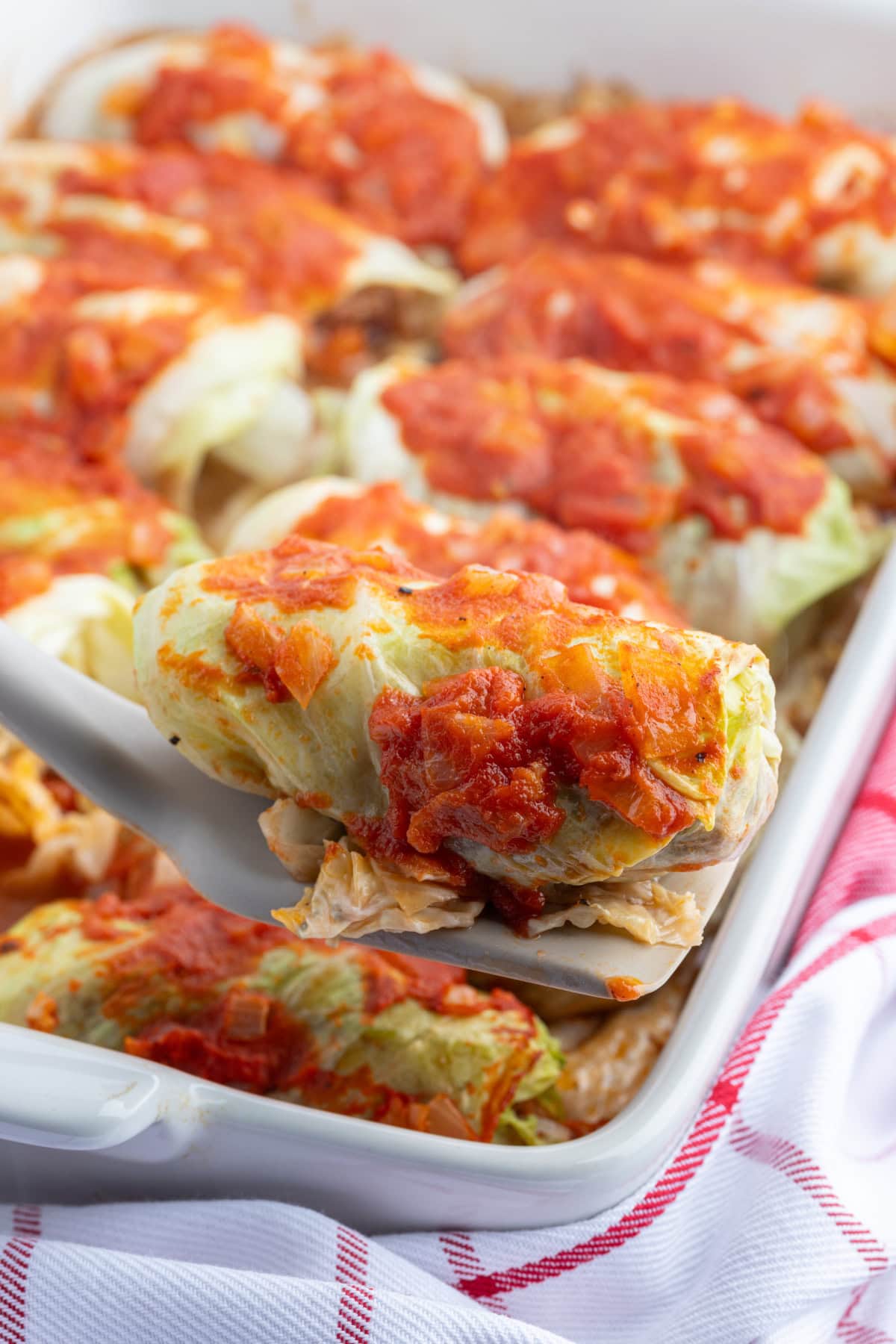 These homemade Polish Cabbage Rolls (Golabki) are the ultimate comfort food! Tender Savoy cabbage leaves are filled with ground beef, rice and seasoned tomato sauce, then baked until tender. Serve with sour cream and applesauce for a delicious old-fashioned family dinner. Save this recipe for a cozy weekend meal! spooning out a serving of polish cabbage rolls