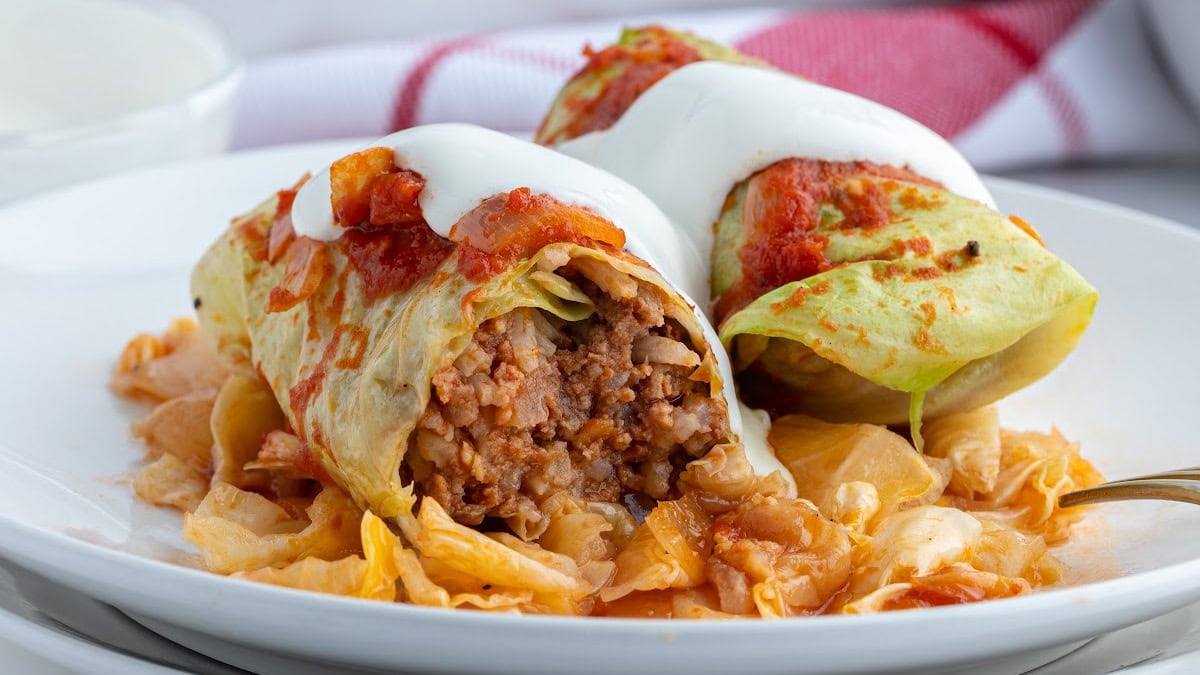 These homemade Polish Cabbage Rolls (Golabki) are the ultimate comfort food! Tender Savoy cabbage leaves are filled with ground beef, rice and seasoned tomato sauce, then baked until tender. Serve with sour cream and applesauce for a delicious old-fashioned family dinner. Save this recipe for a cozy weekend meal! polish cabbage rolls on plate cut open to see inside and topped with sour cream